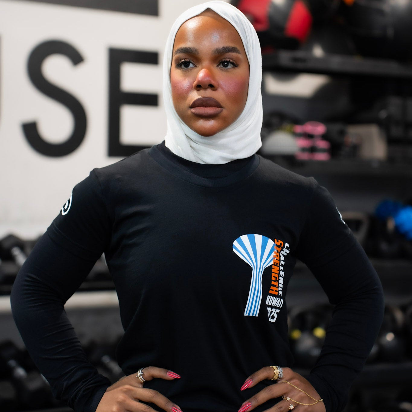 Person wearing a black long-sleeve shirt with a logo, standing in a gym setting.