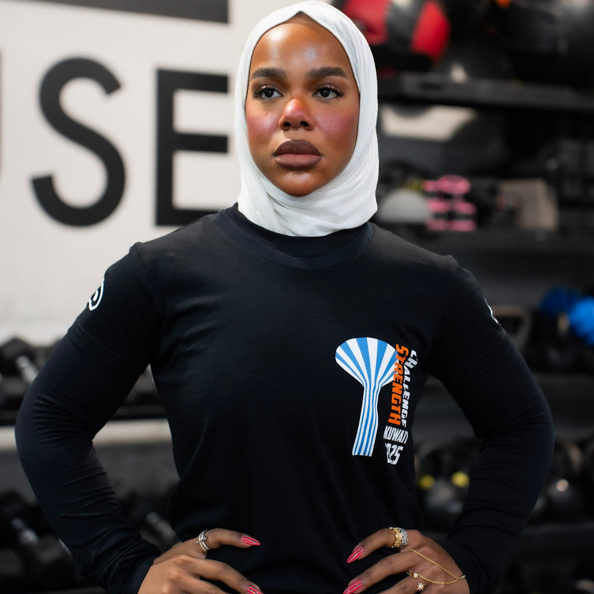 Person wearing a black long-sleeve shirt with a logo, standing in a gym setting.